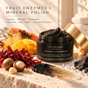 La Fervance Gommage Extraordinaire fruit enzymes and mineral polish jar with its gold lid resting beside it, styled on a stone surface with papaya, mango, pineapple, red seaweed, nuts, and a smear of the black polish.
