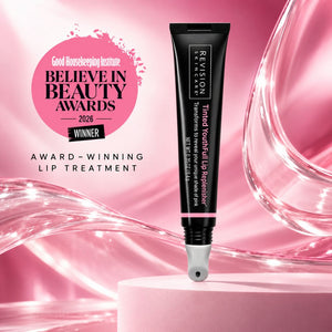 A black tube of Revision Skincare Youthful Lip Replenisher with pink text, standing on a pink pedestal against a pink glossy background. A pink award badge on the left reads 'Good Housekeeping Institute Believe in Beauty Awards 2026 Winner'.