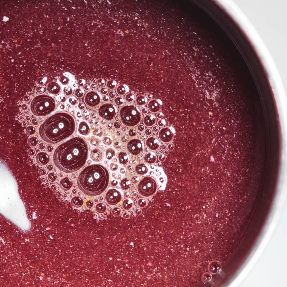 A close-up view of Skin Integrate 28 Biome Poweder mixed up inside a white bowl, featuring a textured surface with a central cluster of bubbles.