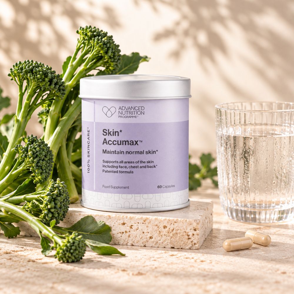 A white supplement jar labeled 'Skin+ Accumax' by Advanced Nutrition Solutions, styled on a stone block with fresh broccoli and a glass of water on a sunlit beige surface.