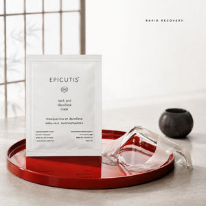Epicutis neck and decolletage mask packaging standing upright on a red tray, with a clear plastic mask partially peeled back and a small dark bowl nearby in a softly lit interior setting.