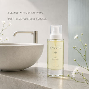 A clear bottle of Epicutis oil cleanser with pale yellow liquid stands on a light stone countertop beside a ceramic sink and small white flowers. Text on the image reads: 'CLEANSE WITHOUT STRIPPING / SOFT.