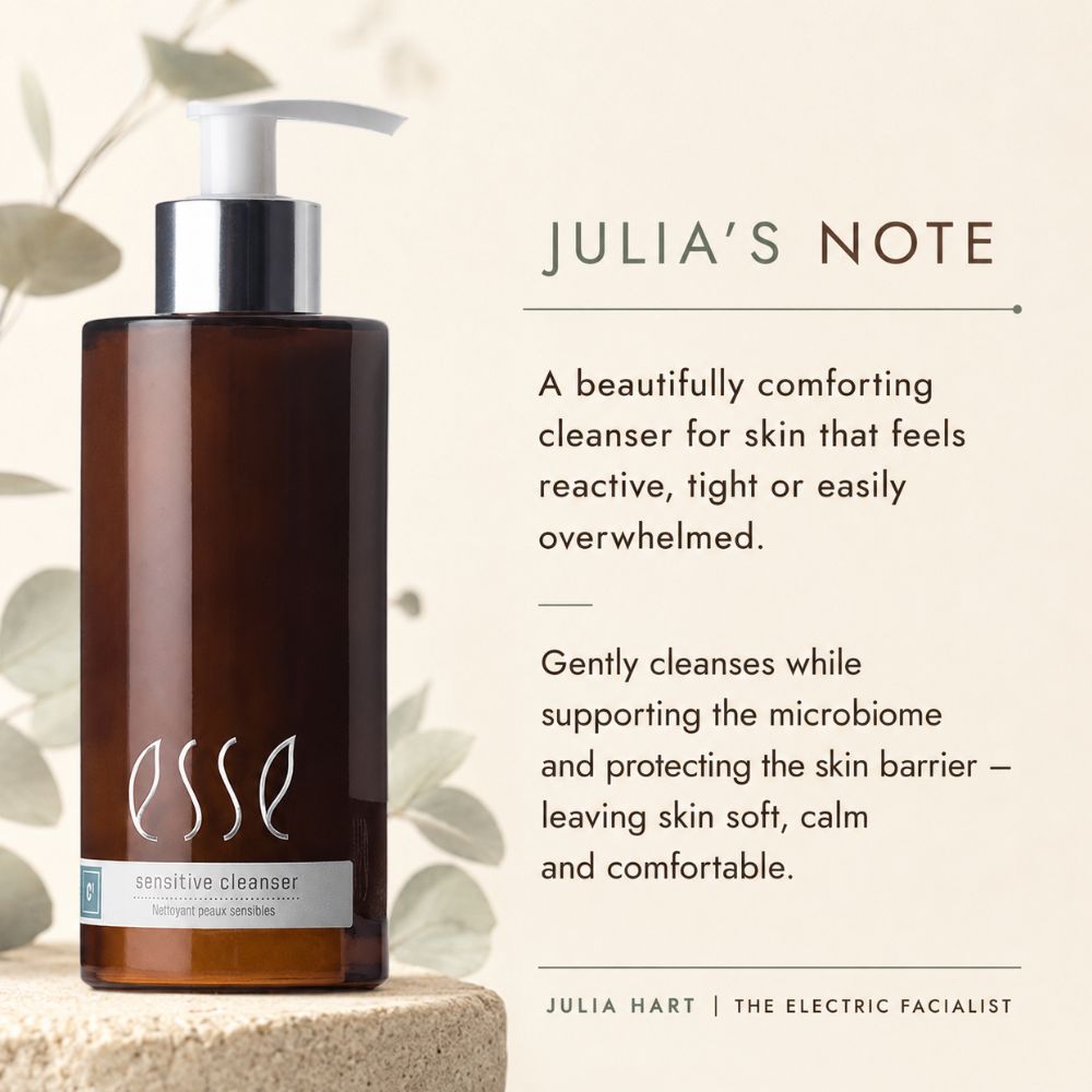 Esse Sensitive Cleanser bottle in a dark amber brown glass with a white pump and silver collar, displayed on a stone pedestal next to descriptive text about 'Julia's Note' on a warm beige background with soft leaf illustrations.