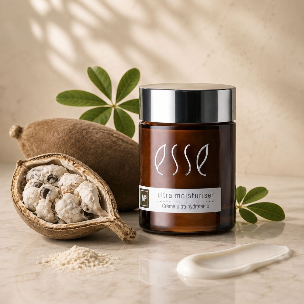 A jar of Esse Ultra Moisturiser cream stands on a marble surface with a scoop of the white cream, a whole and halved brown seed pod, and green leaves in the background, creating a natural, organic aesthetic.