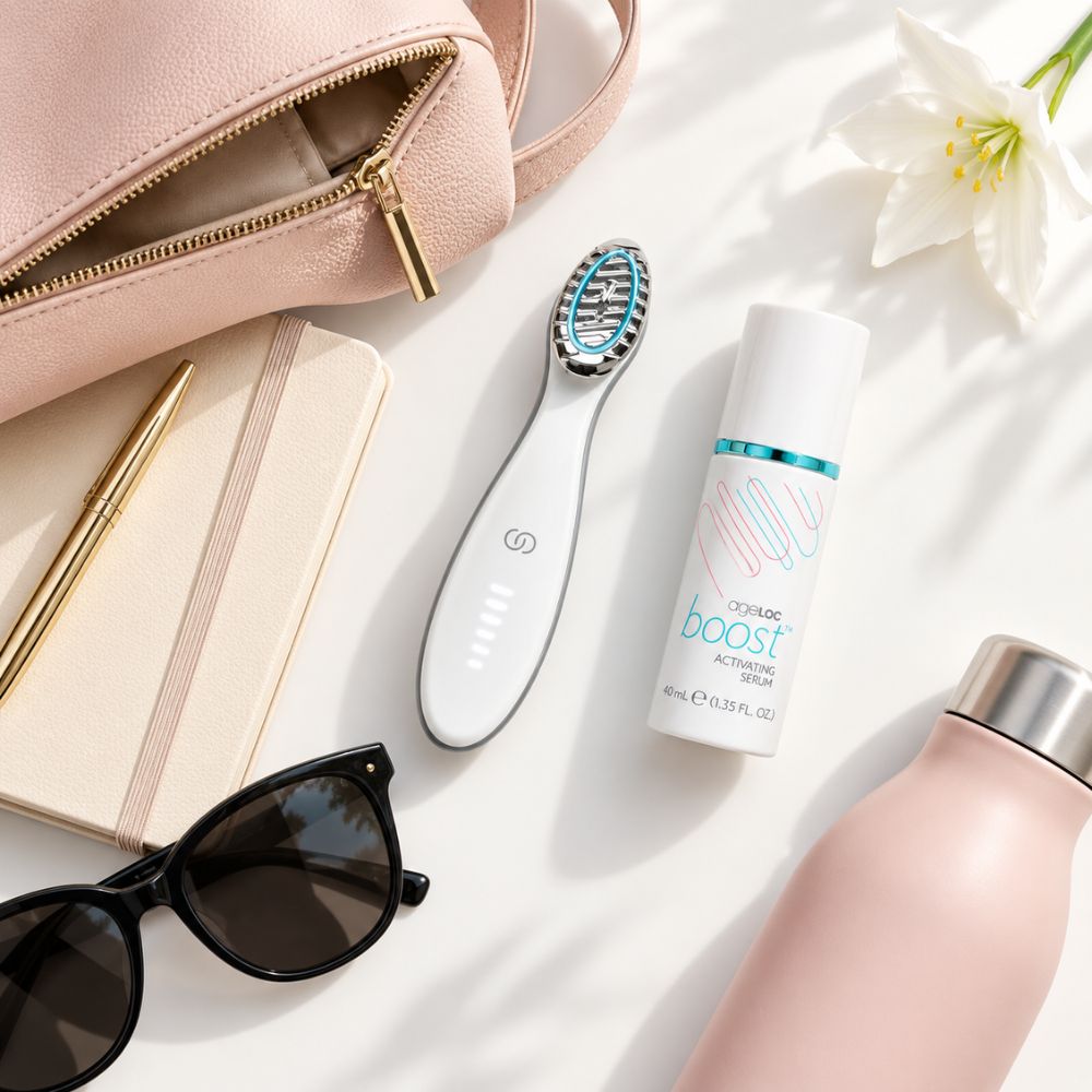 A flat-lay arrangement featuring a Nu Skin ageloc Boost Activating Serum bottle, styled with a pink leather zip pouch, a notebook, sunglasses, a pen, a flower, and a pink bottle on a white surface with soft shadows.