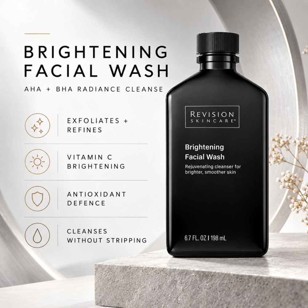 Revision Skincare Brightening Facial Wash in a matte black bottle, displayed on a stone pedestal next to product benefits text on a light gray background.