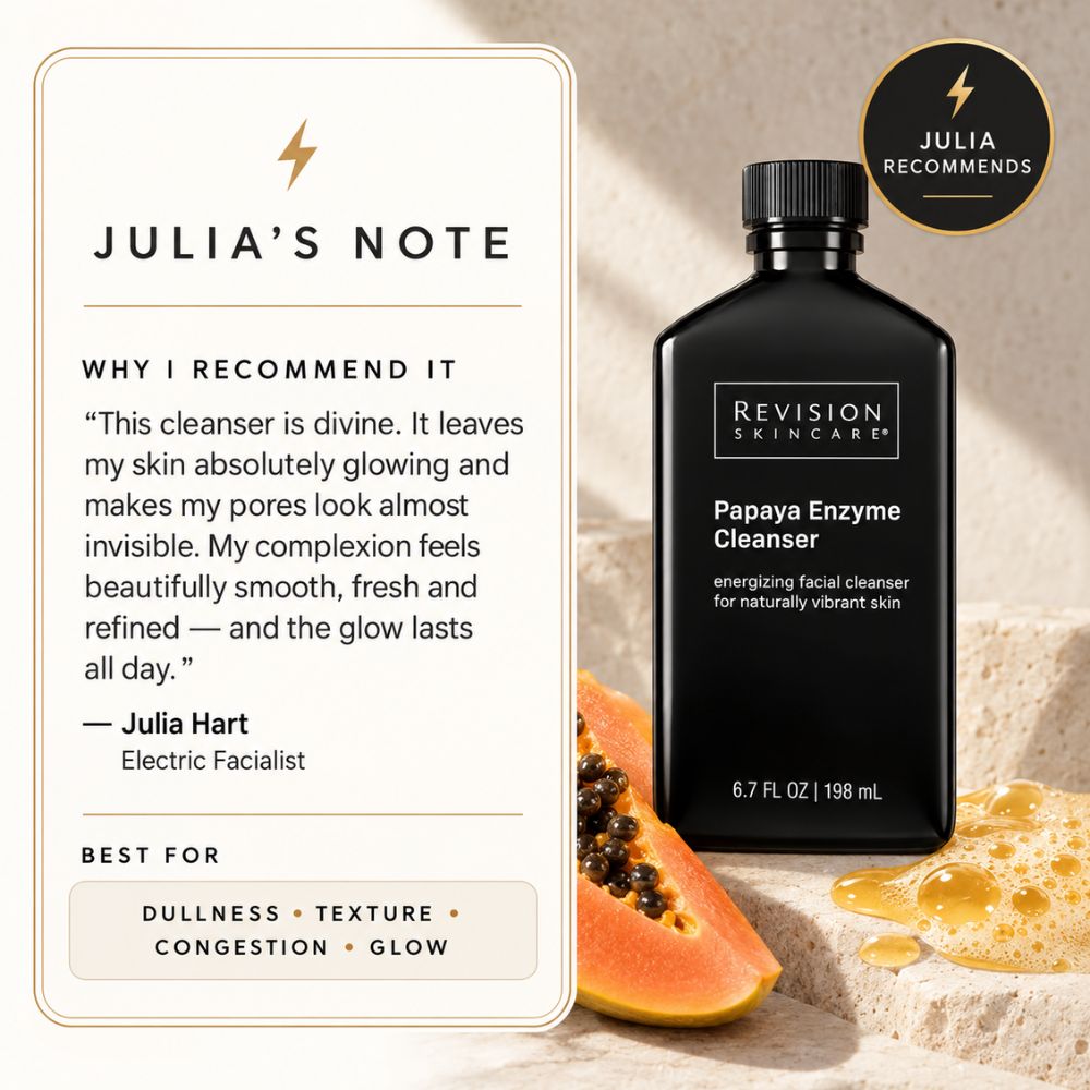Revision Skincare Papaya Enzyme Cleanser bottle in black packaging, shown beside a cream-colored card labeled 'Julia's Note' with a recommendation quote from Julia Hart. The scene includes papaya slices and honey on a textured beige surface, with a circular 'Julia Recommends' badge.