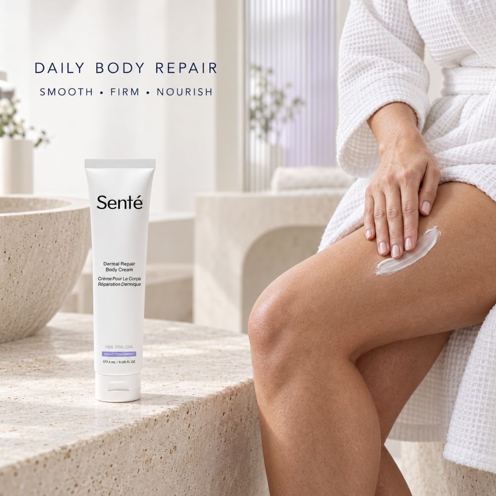 A tube of Sente Dermal Repair Body Cream stands on a stone surface beside a woman in a white robe sitting on a bench, with cream smeared on her thigh. The scene is softly lit and styled in a bathroom-like setting.