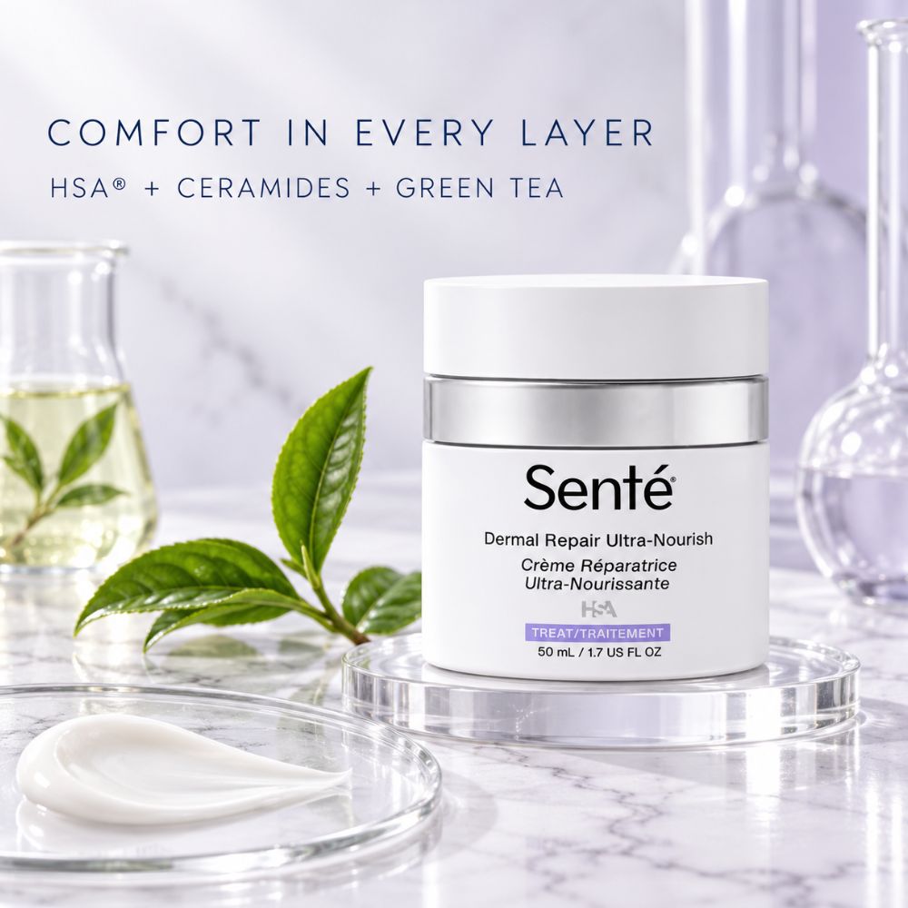 Sente Dermal Repair Ultra-Nourish cream jar on a clear acrylic stand, with a white spoon of cream in the foreground, green tea leaves, and glassware in the background under the text 'COMFORT IN EVERY LAYER'.