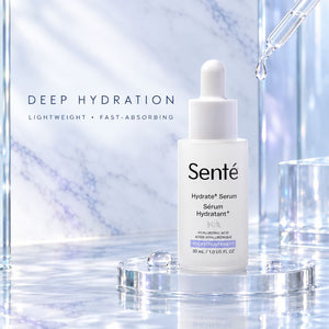Sente Hydrate+ Serum in a white dropper bottle, displayed on a clear acrylic stand with a glass dropper and marble-textured background.